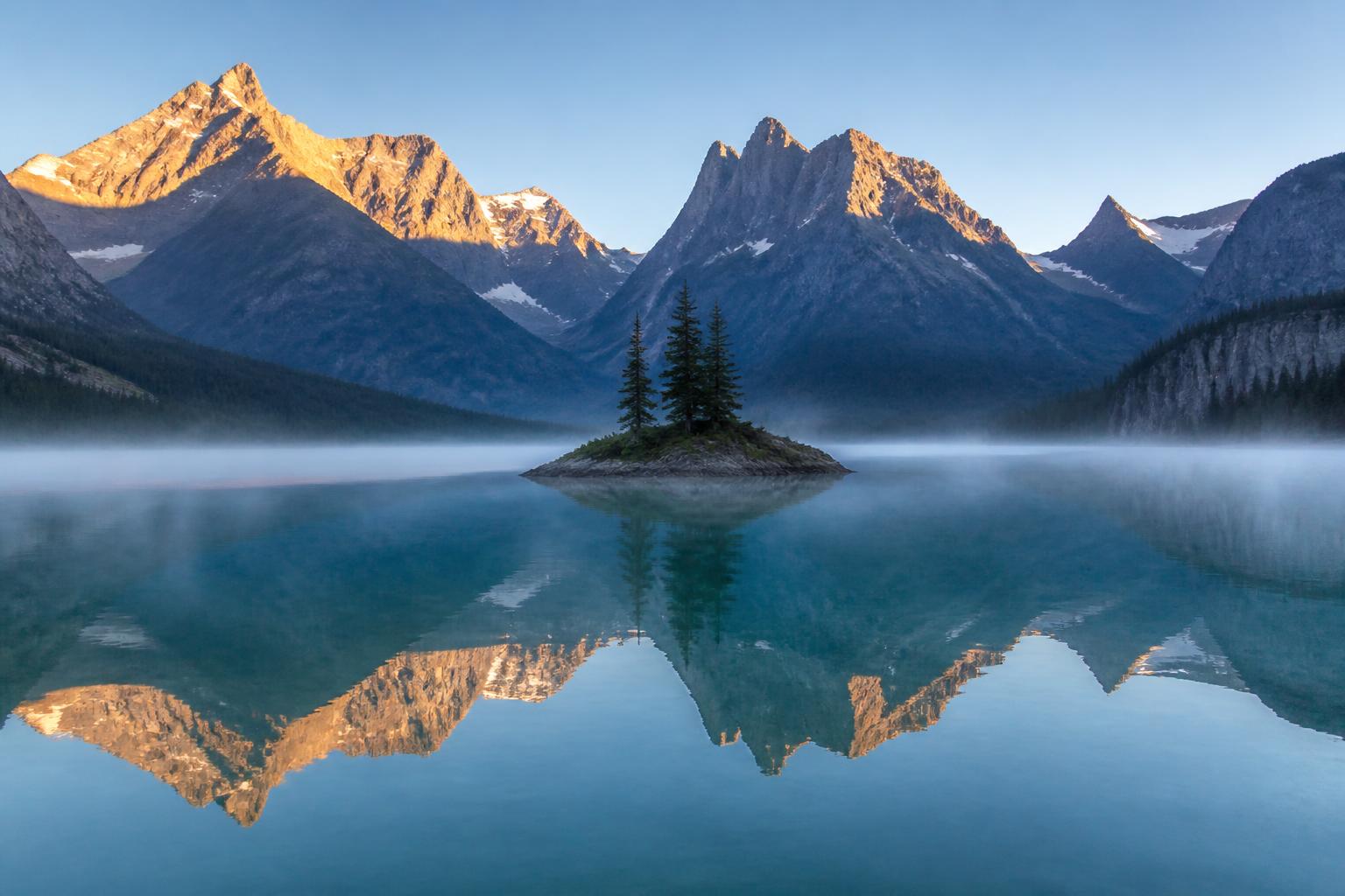 Postal panorámica del Wild Goose Island en el lago St. Mary al amanecer con la pequeña isla rocosa en el centro del lago y la cadena de las Rocky Mountains de Montana detrás, agua turquesa y reflejos