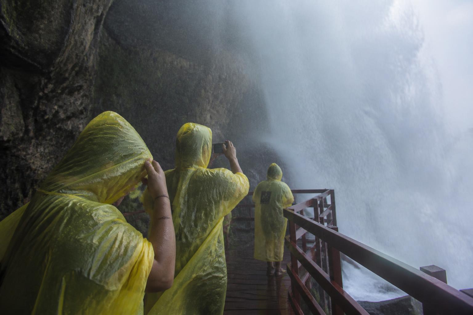 Plataforma de madera del Cave of the Winds con turistas en ponchos amarillos a metros del agua de Bridal Veil Falls, agua salpicando y vapor de la catarata alrededor