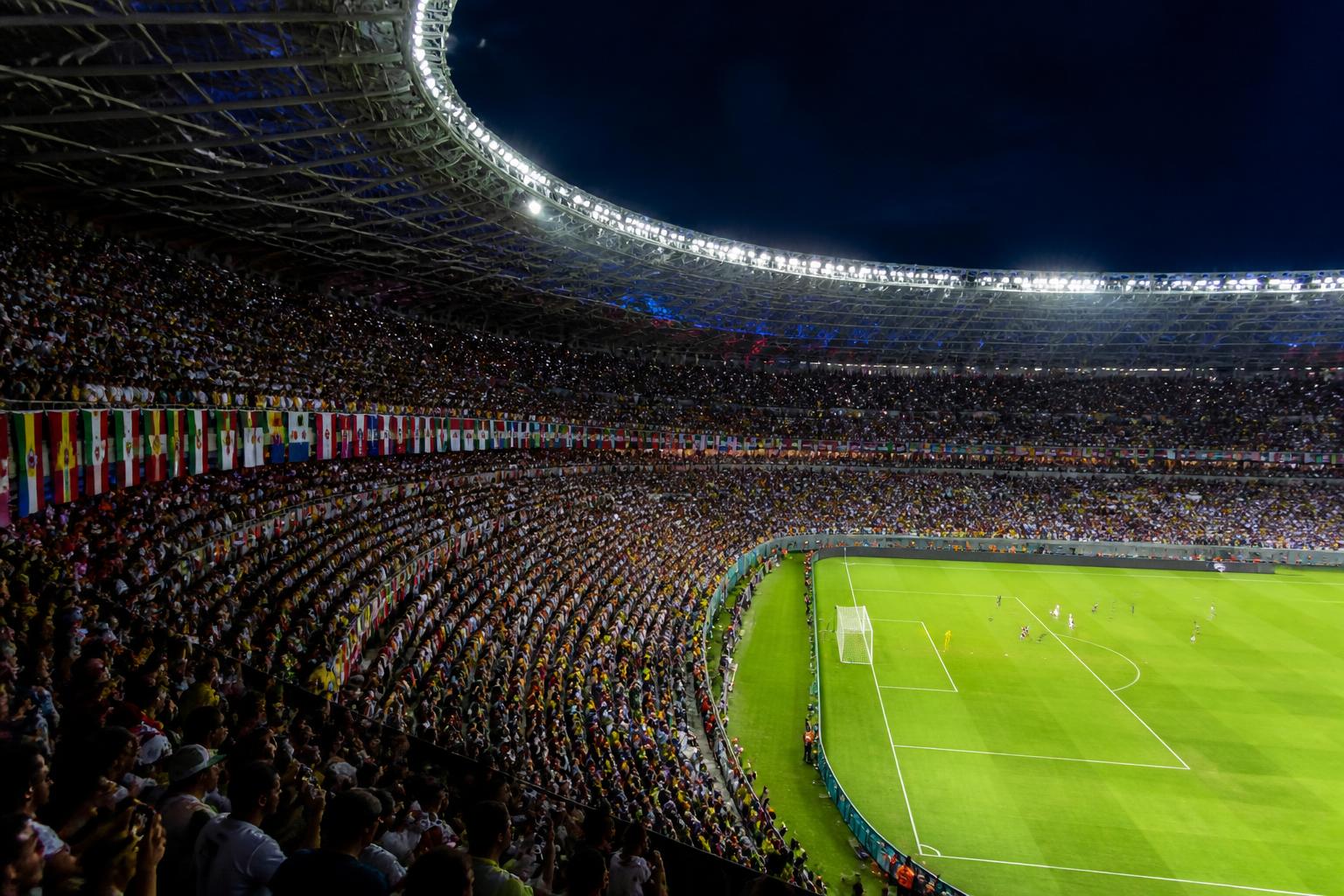 Multitud llenando MetLife Stadium en una noche de verano con la cancha iluminada y banderas de selecciones del Mundial 2026 colgando de las tribunas superiores